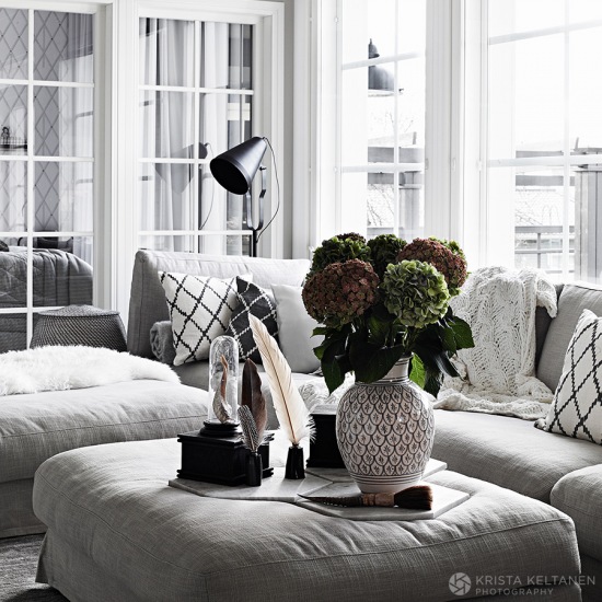 Białe drewniane witryny w salonie skandynawskim z jasno-szarymi nowoczesnymi sofami i pufami,piękne hortensje w dekoracji wnętrz