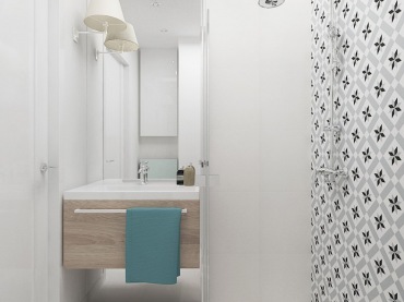 Niewielką łazienkę w kawalerce wypełnia biel, od podłogi do sufitu, oraz akcenty jasnej szarości. Elementem dodającym żywiołu we wnętrzu jest z pewnością wzorzysta ściana po stronie prysznicowej. Kolorowy ręcznik także urozmaica skandynawską...