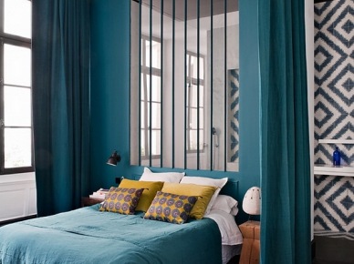 Ciemno-turkusowe zasłony i sciana z lustrzanymi listwami w aranżacji nowoczesnej sypialni z turkusową narzutą,żółtymi poduszkami i grafitową podłogą z desek (26191)