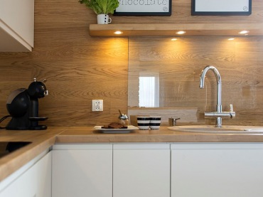 Drewniana ściana w kuchni pięknie komponuje się z dominującą bielą. Gładkie fronty szafek podkreślają prostotę stylu...