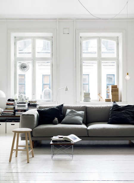 Biały salon z szarą sofą ubraną w czarne poduszki