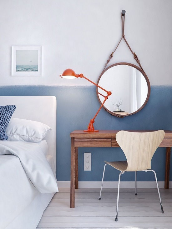 Okrągłe lustro skandynawskiw,czerwona lampka przy łóżku,biało-niebieska ściana i drewniany stolik w sypialni