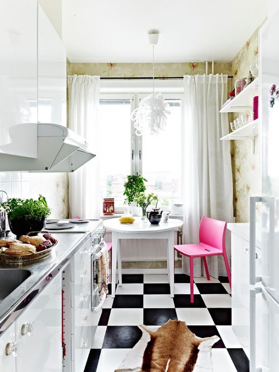 Biała mała kuchnia z różowym krzesłem iczarno-białą posadzką