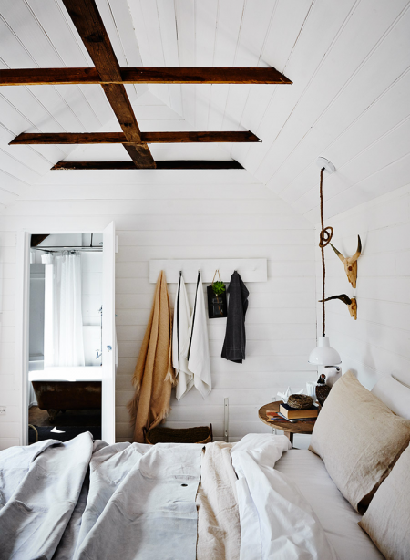 Brązowe drewniane belki w białej sypialni,okrągły stolik z drewna,lniana pościel