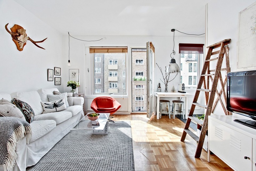Aranżacja białego salonu skandynawskiego z drabiną,porożem jelonka i czerwonym fotelem