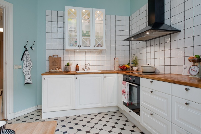 Biała kwadratowa glazura na turkusowej ścianie w białej kuchni skandynawskiej z czarnym okapem i bialo-czarną terakotą na podłodze