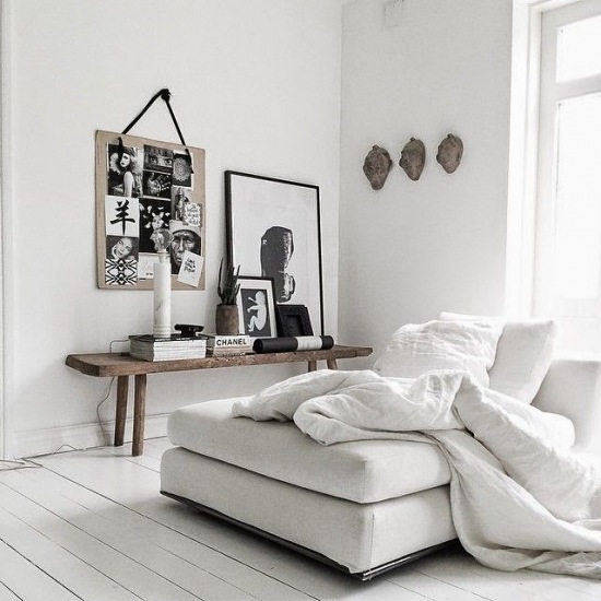 Biała podloga z desek,białe ściany i biała sofa w aranżacji skandynawskiego salonu z drewnianą ławką i czarno-białymi fotografiami i grafikami