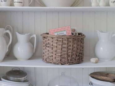 Na półkach ustawiono jasne naczynia, dekorując w ten sposób subtelnie wnętrze. Koszyk z wikliny i naturalne drewno...