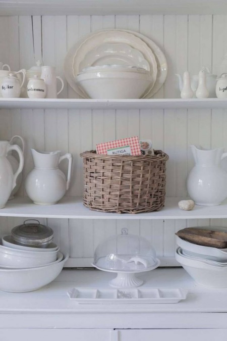 Białe naczynia i wiklinowy koszyk jako dekoracje w kuchni