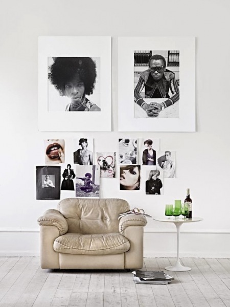 Czarno-białe fotografie w antyramach na białej ścianie w nowoczesnej aranżacji ze skórzanym fotelem i bialym okragłym stolikiem
