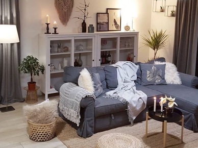 Na szarej sofie leżą koce i poduszki, które podkreślają ciepły charakter salonu. Ustawiona pod ścianą witryna pozwala na przechowywanie bardziej ozdobnych elementów...