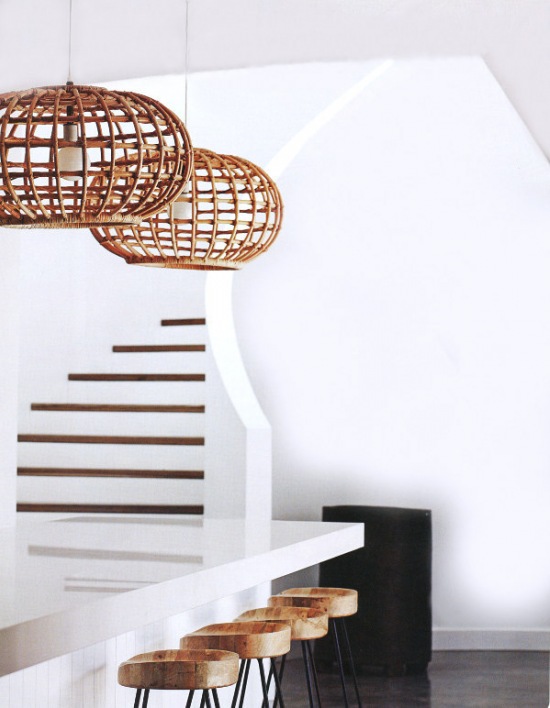Ażurowe lampy z bambusa nad biała lada kuchenną przy białych schodach z drewnianymi opaskami