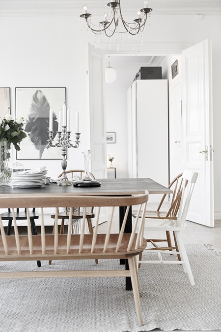 Skandynawska drewniana ławka przy stole na kozłach w białej jadalni z nowoczesnymi grafikami na ścianie