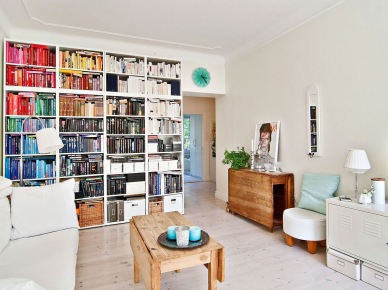 Zabudowa biblioteczki w salonie z drewnianymi składanymi stołami i turkusowym zegarem nad drzwiami (24569)