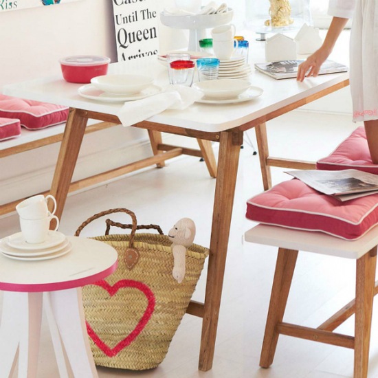 Skandynawski stół i ławki z drewnianymi blatami,różowe poduchy siedziska i pleciony koszyk z różowym sercem