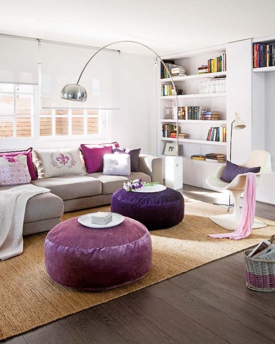 Srebrna lampa podłogowa na pałąku,fioletowe okragle pufy,różowe poduszki i nowoczesne foteliki w salonie