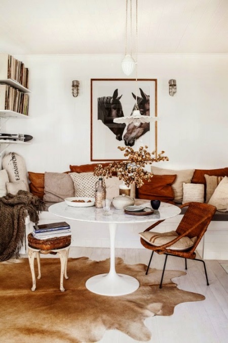 Metalowy fotel z bambusową plecionką,okragły biały stół na jednej nodze,stylowy taboret,sofa z biało-rudymi poduszkami,nowoczesna fotografia,eklektyczny salon z kominkiem,stylowy mix w salonie,biało-brązowa aranżacja salonu w eklektycznym s