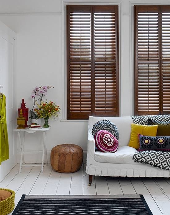 Drewniane shuttersy,żółte poduszki,biała podłoga z desek i marokański puf ze skóry