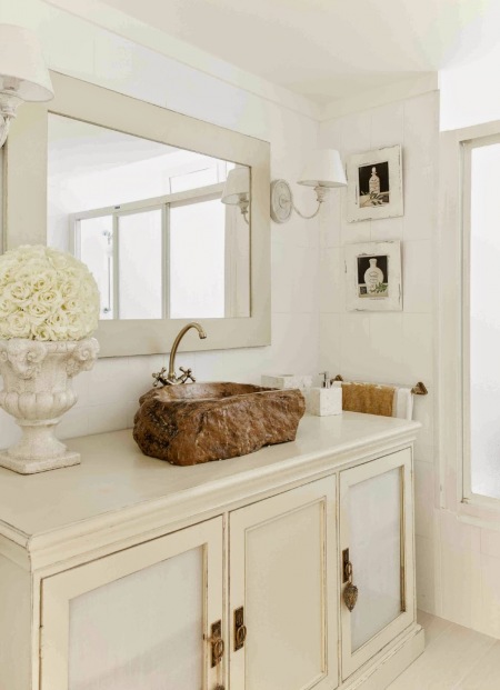 Brązowa kamienna umywalka,białe prostokatne lustro,prowansalskie kinkiety i kamienny biały gazon w łazience