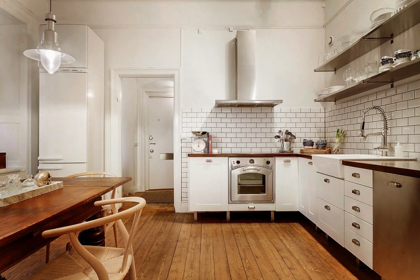 Biała kuchnia w stylu skandynawskim z drewnianymi blatami, podłogą z desek i drewnianym stołem w brązowo-miodowym kolorze