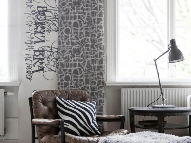 Graficzne wzory tapet w aranzacji skandynawskiego salonu ,czarny drewniany fotel ze skórzana tapicerką,kwadatowy puf z szarym futrzakiem i okragły czarny stolik kawowy (25992)
