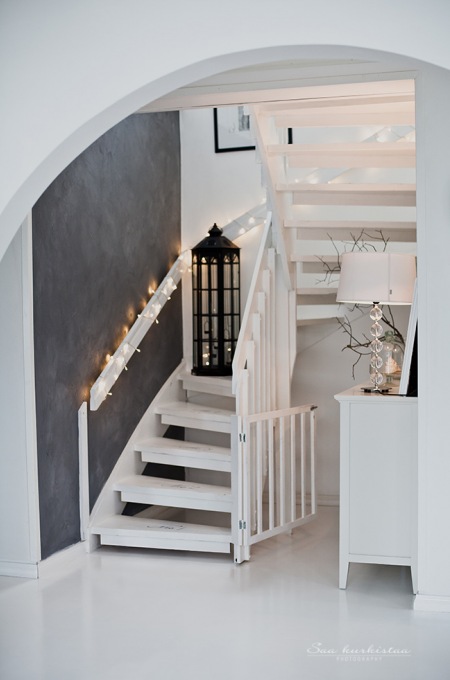 Szara ściana, lampion i girlanda z żarówkami w aranżacji białych schodów
