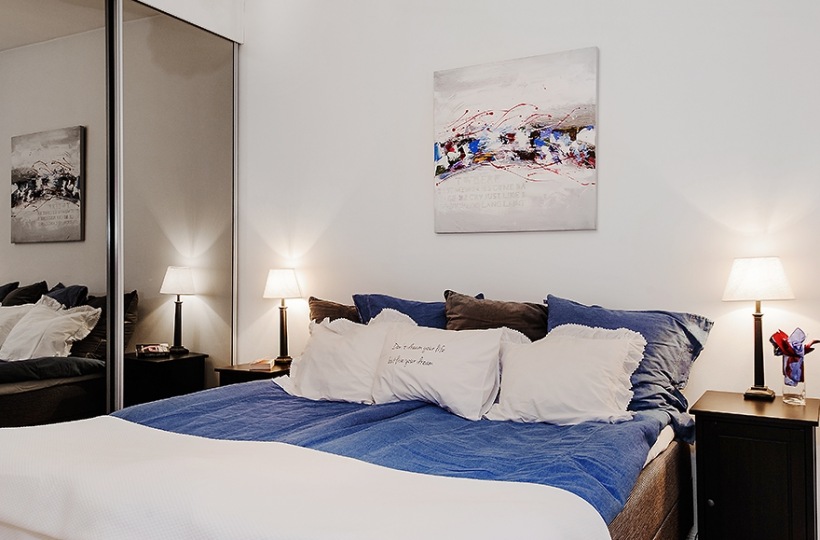 Lustrzane szafy i biało-niebieskie detale w skandynawskiej sypialni w sypialni