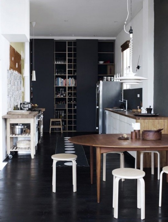 Czarna ściana w kuchni , czarna podłoga,dreeniany owalny stół z białymi taboretami w skandynawskiej kuchni