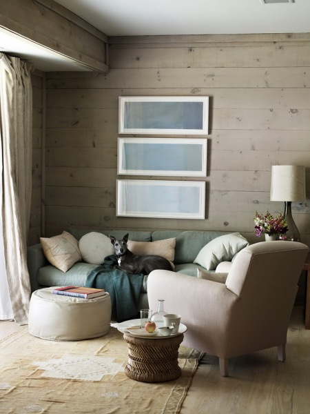 Szaro-beżowe deski na ścianie i podłodze,mietowa sofa,szmaragdowy pled i biały okrągły puf w salonie