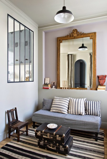 Okno w ściance działowej,stylowe lustro złote,walizki vintage i prosta kanapa poduszlami w niebiesko-biale paski