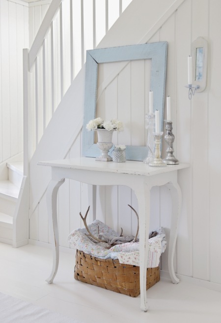 Biała postarzana konsolka z drewna i niebieskie lustro vintage  przy białych schodach