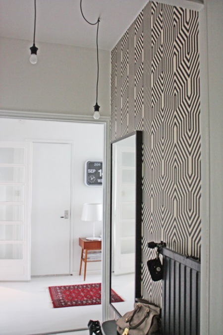 Biało-czarna graficzna tapeta na scianie w przedpokoju z czarnym prostokatnym lustrem i żarówkami na kablach