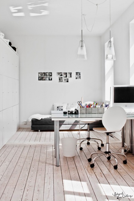 Pokój biurowy z białymi szafami w wysokiej zabudowie,szklanymi lampami i nowoczesnym biurkiem na metalowych nogach