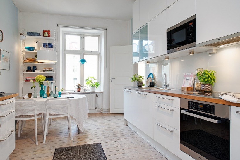 Biała nowoczesna kuchnia z drewnianymi blatami,biały stół z krzesłami i białe wiszące półki na ścianie w dekoracji kuchni