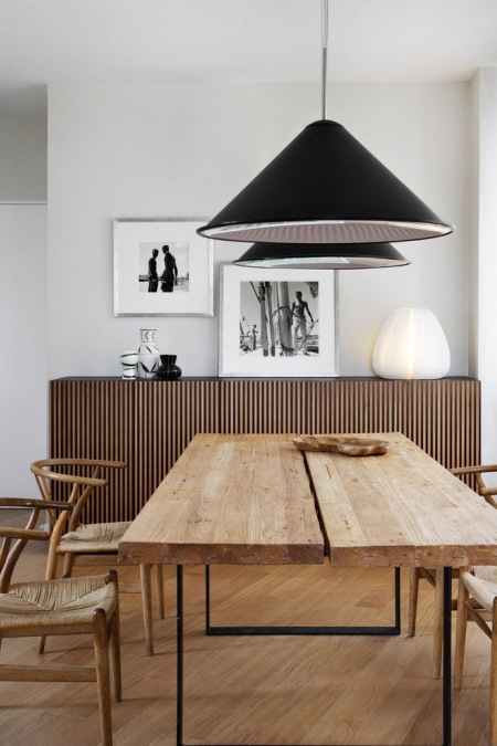 Drewniany gruby blat i metalowe podpory w industrialnym stole w jadalni z czarnymi stożkowymi lampami , giętymi krzesłami z drewna i juty i drewnianymi nowoczesnymi komodami z drewna