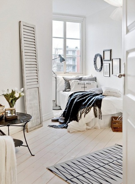Drewniane bielone drzwi vintage jako dekoracja w sypialni z metalowym stolikiem tacą,skandynawski dywanikiem i ozdobnymi ramami w domowej galerii grafik na ścianie,