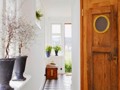 Białe ściany,białoczarna terakota cementowa ułożona w karo,czeresniowe drzwi z okragłym oknem w stylu vintage,drewniana skrzynia,czarne amfory z kamienia (26001)