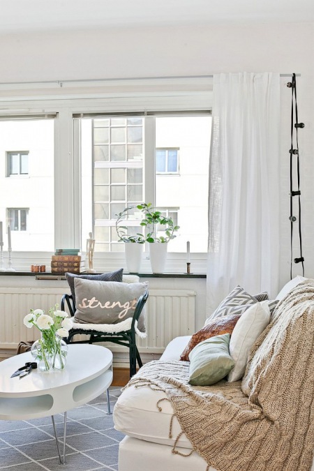 Beżowy dziergany koc,miętowa poduszka,białe zasłony,czarna girlanda z żarówek w salonie w stylu skandynawskim