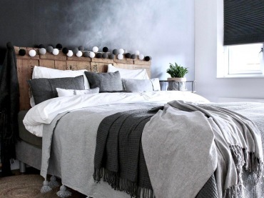W sypialni wezgłowie łóżka tworzą drewniane deski, na których szczycie przymocowano drobną girlandę z szarych i białych...