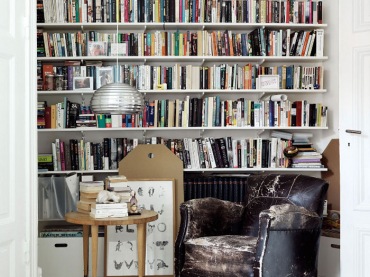 Półki z książkami od podłogi do sufitu, fotel skórzany vintage i skandynawski stolik okragły w aranzacji domowej biblioteki (22393)