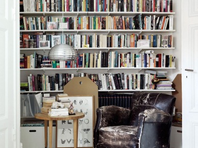 Półki z książkami od podłogi do sufitu, fotel skórzany vintage i skandynawski stolik okragły w aranzacji domowej biblioteki (22393)