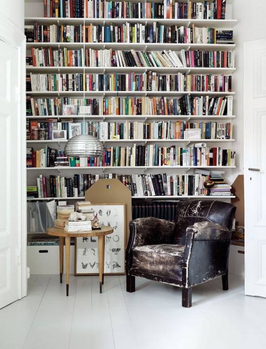 Półki z książkami od podłogi do sufitu, fotel skórzany vintage i skandynawski stolik okragły w aranzacji domowej biblioteki