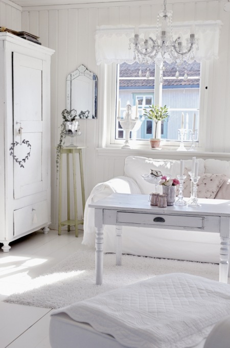 Żyrandol z białymi krryształkami,biała rustykalna szafa,biała kanapa,skandynawski stolik z szufladą i wysoki kwietnik z naturalnego drewna