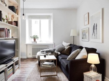 Grafitowa sofa, drewniana postarzana podłoga i biały regała z TV i książkami w małym salonie (24439)