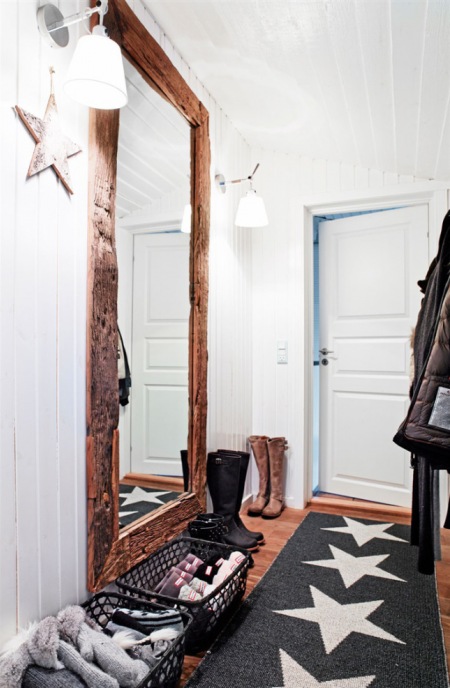 Duże prostokątne lustro z drewna na ścianie w wąskim przedpokoju z szarym dywanem w białe gwiazdki
