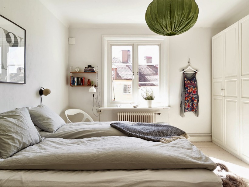 Zabudowa białych tradycyjnych szaf w sypialni z szarą pościelą i zielonym abażurem z tkaniny w wiszącej lampie