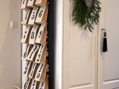 Adwentowy kalendarz z papierowych torebek na białej szafie z zieloną gałązką świąteczną (27331)