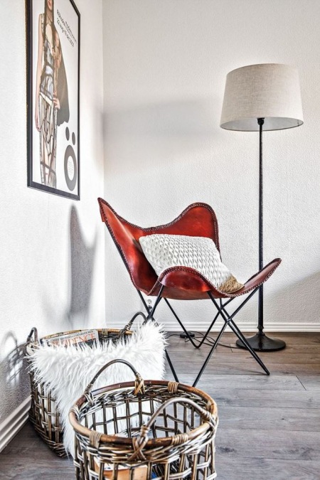 Skórzany brązowy fotel butterfly,nowoczesna grafika na białej ścianie,wiklinowe ażurowe kosze,drewniana podłoga z bielonych desek
