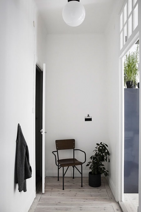 Industrialne metalowe krzesło,białe ściany,czarne drzwi w otwartym przedpokoju w mieszkaniu