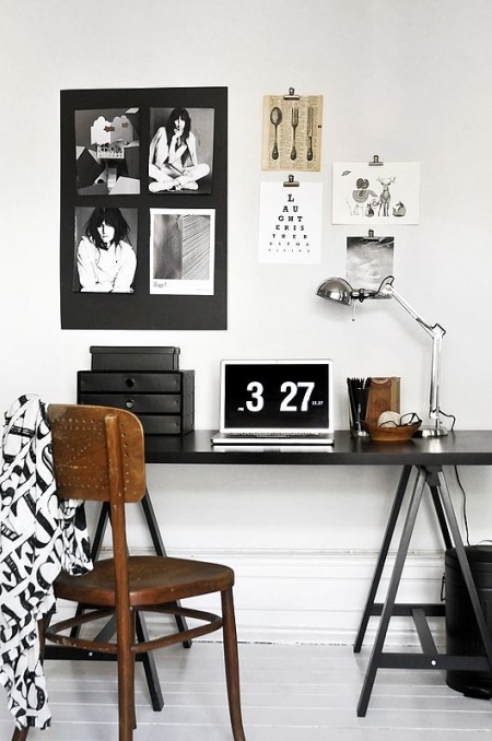 Czarne biurko na kozlach w stylu skandynawskim,czarne pudelka na biurowe akcesoria,metalowa lampka biurkowa,czarna tablica z fotografiami, i drewniane krzesło przy biurku